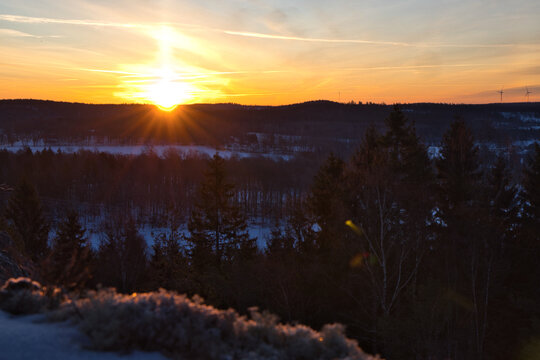 Golden sunrise bursting over a snowy winter forest in Dalsland, Sweden, with vibrant sun rays illuminating a frozen landscape and pine trees under a warm orange and yellow sky
