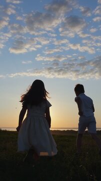Adorable siblings, a boy and a girl, holding hands while running through a grassy field towards the horizon during a beautiful, warm sunset, enjoying a happy and carefree childhood moment