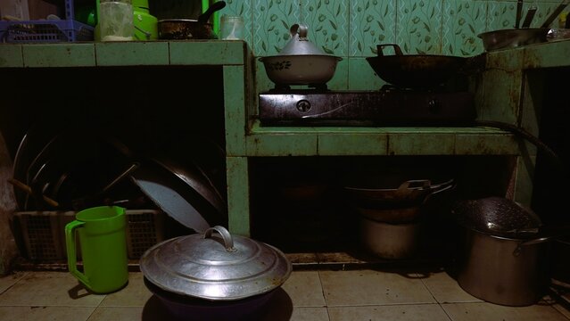 Dirty kitchen with messy metal pot utensils, unhygienic lifestyle, Rustic kitchen interior with traditional stove and various metal cooking pots and pans.