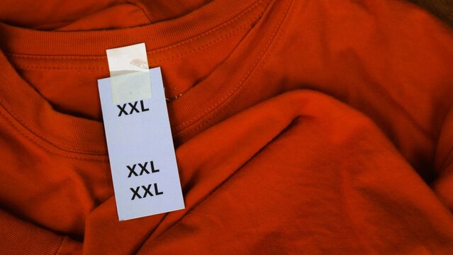 Close up of an orange t-shirt with a large size label tag attached.