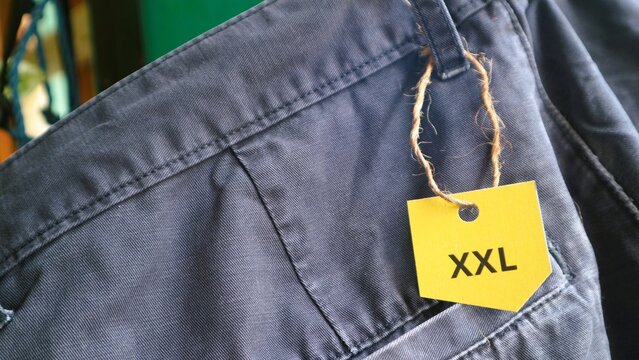 Close up of a pair of dark blue trousers with an XXL yellow size tag.