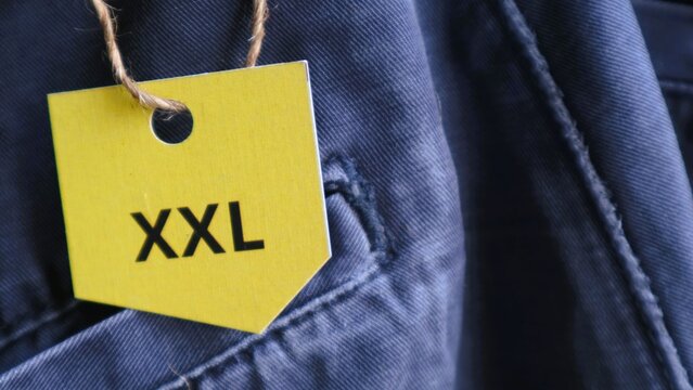 Yellow XXL size clothing label attached to blue denim fabric.