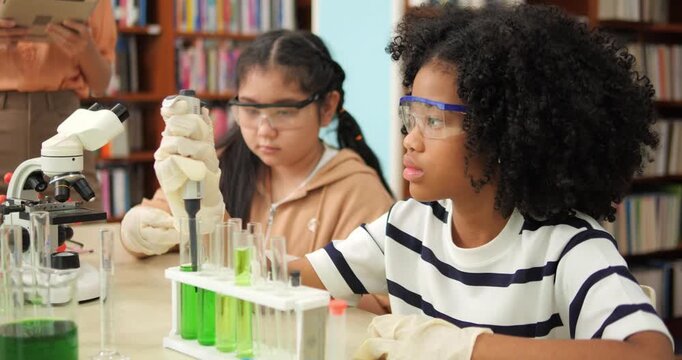 Young students wear gloves and goggles while handling lab equipment. Children examine green liquids in test tubes with focused curiosity