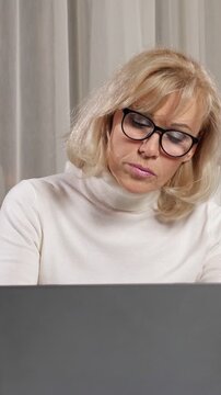 Concentrated senior businesswoman with blonde hair wearing eyeglasses typing on a laptop and working diligently in her office, showcasing focus and professional dedication