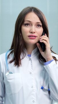Confident female physician in a white coat with a stethoscope talking on her mobile phone, providing a medical consultation or discussing patient care in a clinical setting