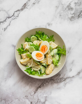 Potato salad with cucumbers, boiled egg and yogurt-mustard dressing on a marble background, top view