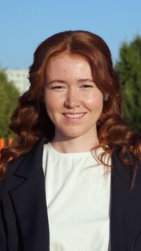 Close up portrait of a lovely young businesswoman with natural red hair and cute freckles smiling genuinely at the camera on a sunny day with a clear blue sky in the background
