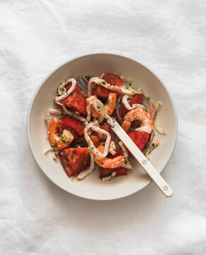 Antipasti salad with fresh tomatoes, squid, shrimp and olive oil on a light background, top view