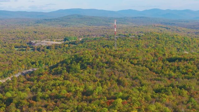AERIAL: Telecommunications tower rises from expansive forest displaying early autumn colours near Otočac, Croatia. Contrasts between modern communication infrastructure and colourful rolling landscape