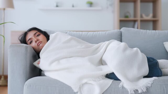 Asian woman resting at home on couch, feeling exhausted after work, lacking energy, or overworked, too tired, and lacking motivation