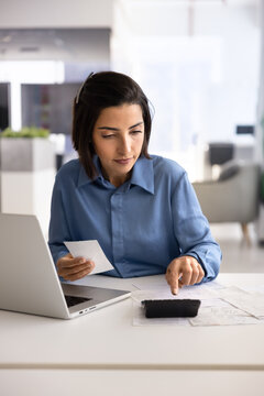 Bookkeeper reviewing expense documents, entering numbers on calculator, calculating receipt, working on financial statements, verifying totals, performing office accountancy tasks at workplace desk