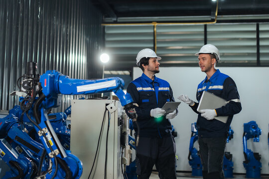 Robotic system integrators inspect customized welding robotic arm in warehouse, supporting robotics system integration, verifying robot programming, calibration, before customer delivery.