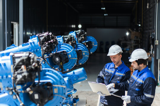 B2B engineering service team inspects refurbished industrial robot arms in warehouse, validating smart manufacturing setup, automation software, precision, reliability, quality before delivery.