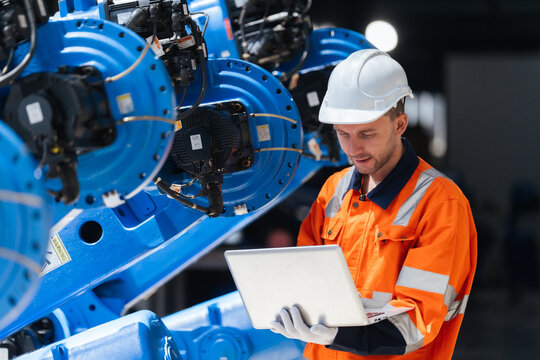Industrial engineer using laptop for software programming supporting robotic system integration, plant engineering, diagnostics, installation