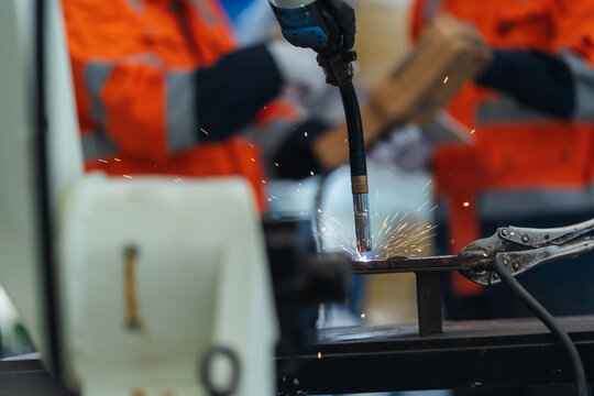 Close-up Welding robot torch operate welding sparks on clamped steel fixture, Robotic welding arm test performs precision welding before delivery.