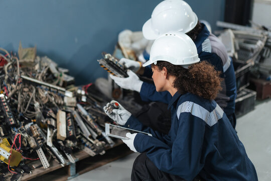 Environmental engineers sort electronic waste and machine parts in factory. using tablet data for waste management, responsible disposal, sustainability management.