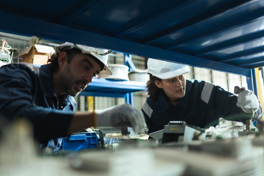 Maintenance Technicians examine robotic arm spare parts under warehouse rack, using tablet for parts identification, inventory control, replacement planning, repair workflow.