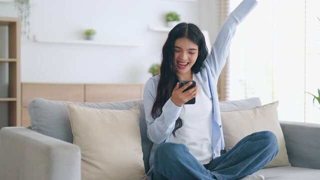 Happy young asian woman relax on comfortable couch at home texting messaging on smartphone, smiling girl use cellphone, chatting online message, shopping online from home