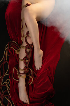 Sensual cropped view of a body bound in artistic Shibari ropes lying on red fabric