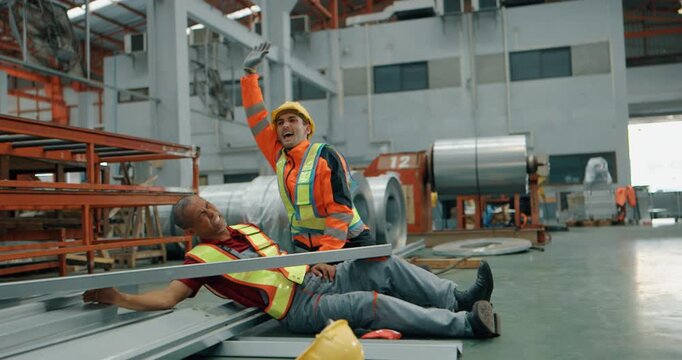 Injured factory worker in pain on floor after accident while colleague helps in steel warehouse