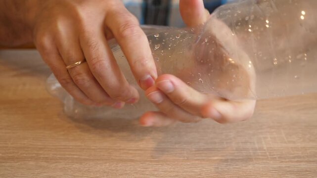 Person intensely crushing an empty plastic bottle by hand in close up on a wooden table. Continuous action with original sound.