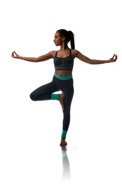 Woman in yoga tree pose wearing athletic wear on white background