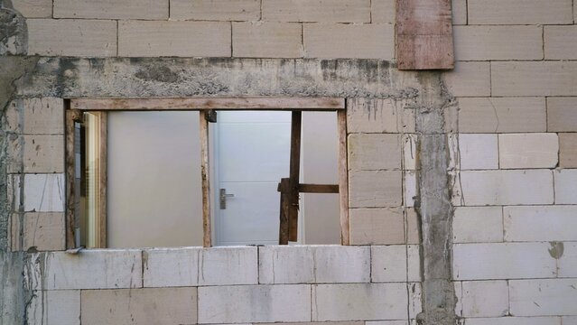 Unfinished brick wall with an open window frame under construction.