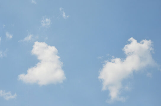 Two fluffy white clouds drifting against a clear blue sky. Peaceful sky with sense of calm and openness on   sunny day .