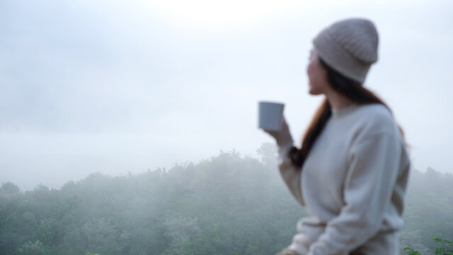 Blurred of a woman drinking coffee while looking at a beautiful foggy mountain and nature view