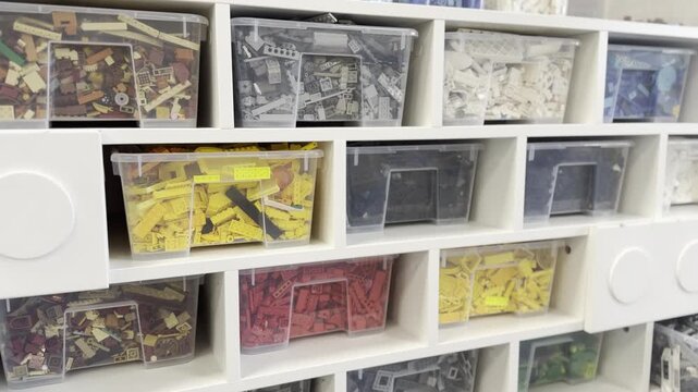 White shelves with clear storage bins filled with sorted colorful toy bricks and parts