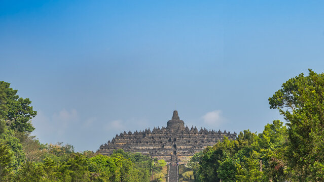 The grandiose ancient temple of Indonesia against the blue sky. It was built like a huge stupa, in the shape of a mandala. Domes, latticed dagobahs, Buddha statues are visible on the tiers. Java. 
 