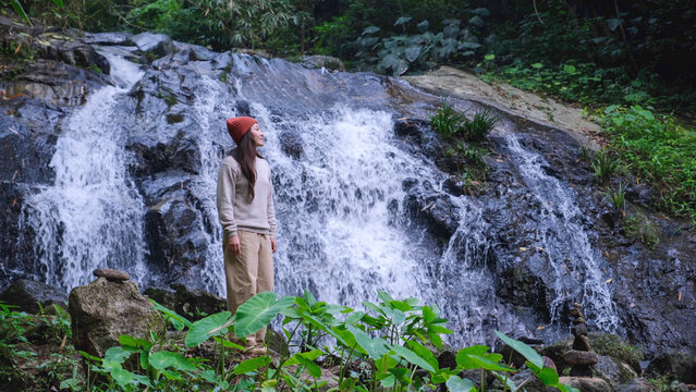 A woman standing and relaxing by the waterfall in the forest