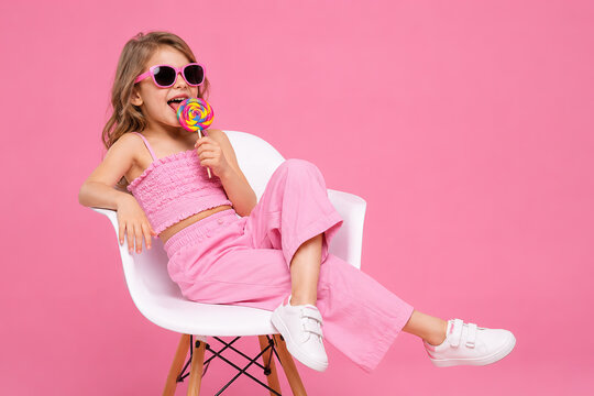 modern fashion girl with a lollipop with chair and pink wall background.