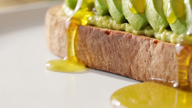 Fresh avocado toast sliced neatly on a white plate with olive oil being poured over it, healthy breakfast, food industry, morning meal, organic eating.