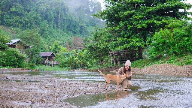 A woman playing with a dog by the river in rural village