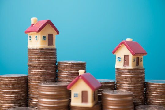 Houses on heap stack coins with blue background. Real estate investment trust (REIT), homebuyer mortgage loan, home finance, reverse mortgage, money management, financial literacy and so on concept.