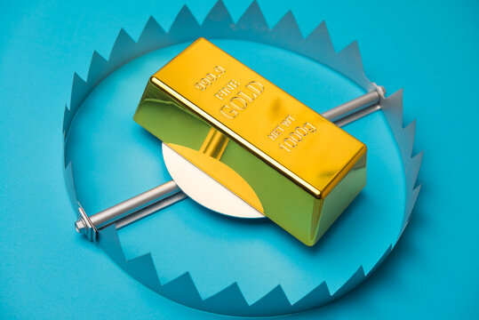 Gold bar in a trap on blue background. High risk in commodity trading market all time high price or online scam investment, crime and so on concept.