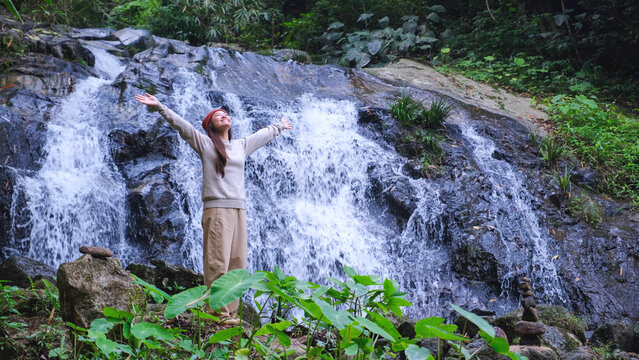 A woman opening arms and relaxing by the waterfall in the forest