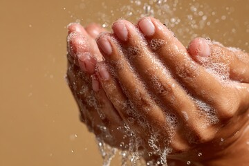 Fototapeta premium Close-up of hands with soap bubbles under running water, showcasing cleanliness and hygiene against a neutral background, emphasizing personal care and sanitation practices