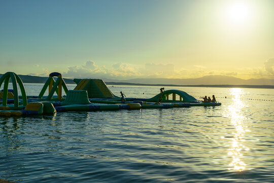 inflatable water park floating on the calm Adriatic Sea during a golden sunset. Warm evening light reflects across the water, creating a relaxing summer holiday atmosphere.