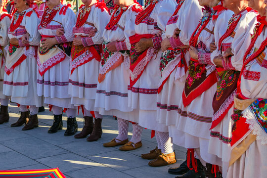 Close-up of women standing arm in arm in authentic Croatian folk costumes with embroidered dresses, floral aprons, and traditional red coral necklaces during Ethno Festival in Selce, Croatia 