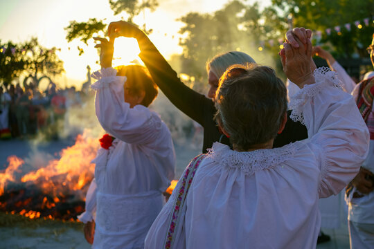 Participants in traditional white folk costumes dancing around a ceremonial bonfire during sunset at the Ethno Festival in Selce, Croatia