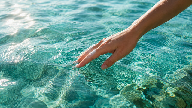 Hand touching clear tropical water. Person reaching into turquoise ocean sea surface.