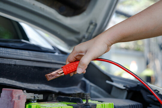 Hand holding jumper cable clamp near car battery