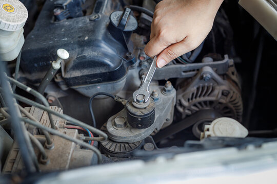 Hand of mechanic using a silver combination wrench to work on a pulley bolt