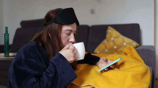 Coffee and social media have become the default morning dopamine as a young woman scrolls her phone in bed creating a habit that can replace a calm mindful start