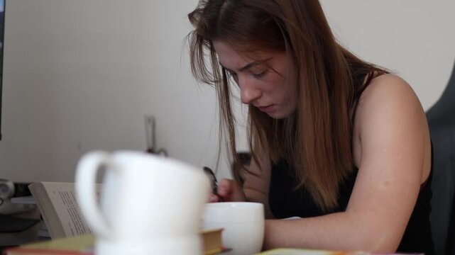 Focused reading replaces distractions as a young woman studies with coffee beside her showing concentration quiet learning and a productive daily routine