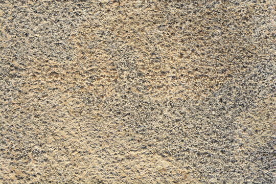 A detailed full frame view shows the rough uneven and weathered surface texture of an old chiseled natural beige stone block.