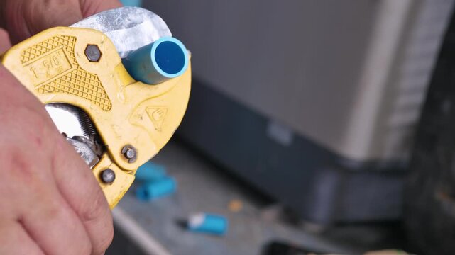 Close-up of a person cutting a PVC pipe with a pipe cutter during a DIY home plumbing repair, preparing plastic pipe for water system installation and maintenance
