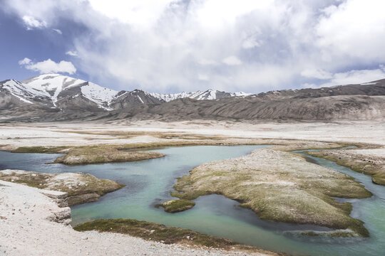 Clear-water rivers and lakes in a mountain valley, pastures and green grassy fields set against mountain ranges and snow-capped, glacier-clad peaks&mdash;a scenic landscape background